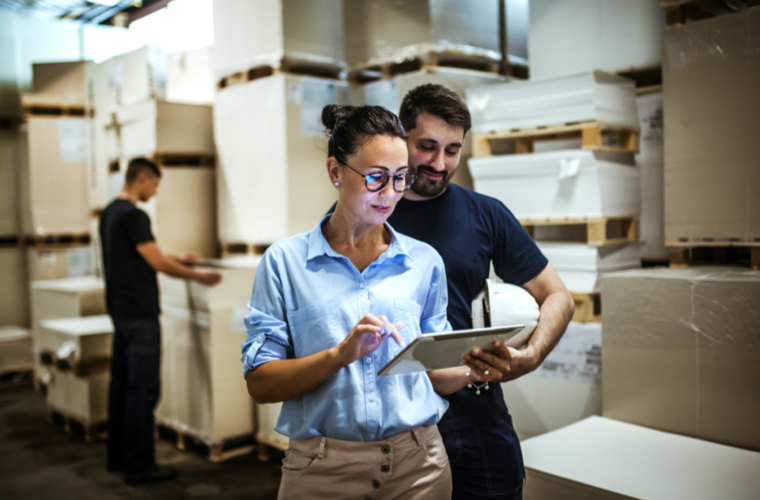Man and woman in a warehouse setting select a health plan on an electronic tablet.